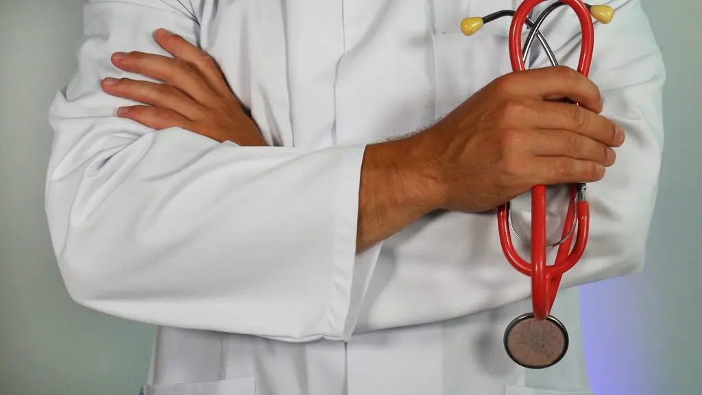 cropped image of a physician's torso holding a red stethoscope on hi left hand while crossed on the other hand