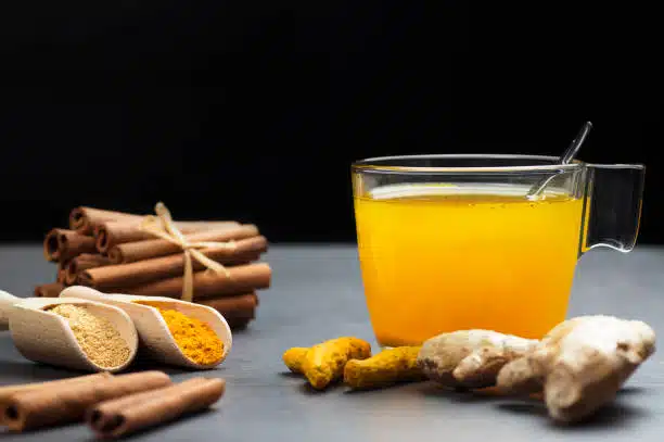 Herbal ginger and turmeric tea in glass cup with ginger root, dry turmeric, cinnamon sticks and their powder. 