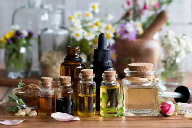 Selection of essential oils with various herbs and flowers in the background.