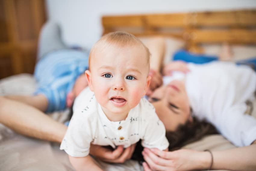 Baby boy with Delayed Milestone crawling on a bed with his parents holding him.