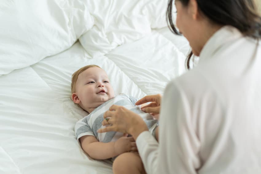 Mother taking care of her baby who suffers from Torticollis while lying on the bed.