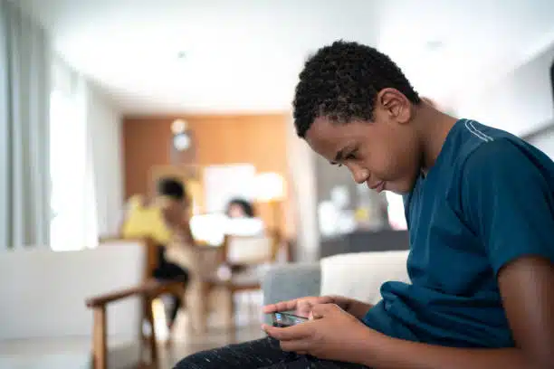 Young boy playing his phone while hunching his back in the sofa.