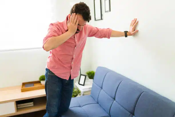 Disoriented man in his 30s feeling dizzy and trying to balance against a wall background. 