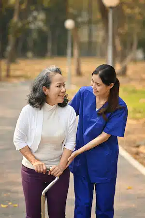 Careful caregiver taking care of elderly woman patient during walking outdoor