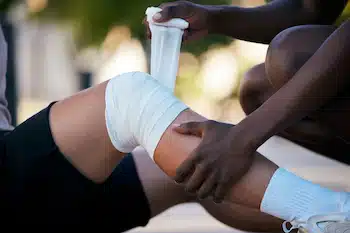 man helping his friend apply first aid bandage on knee after a sport injury