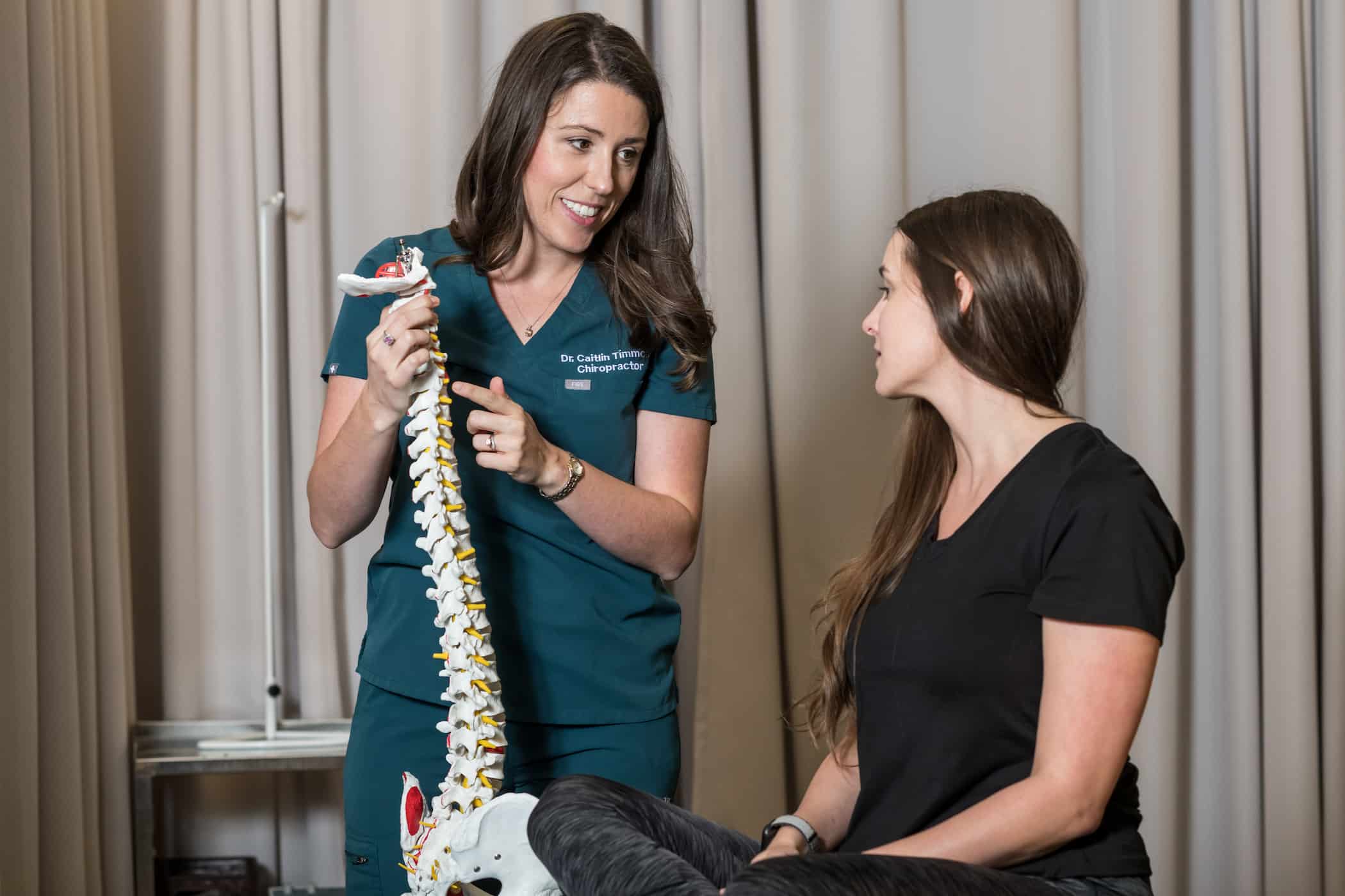 A chiropractor pointing out details on a spine model to a patient.