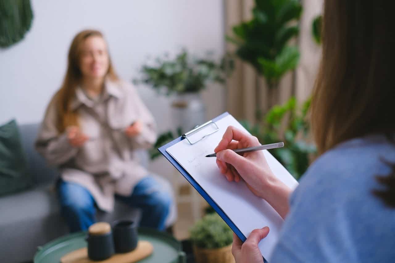 Healthcare professional taking notes during mental health consultation.