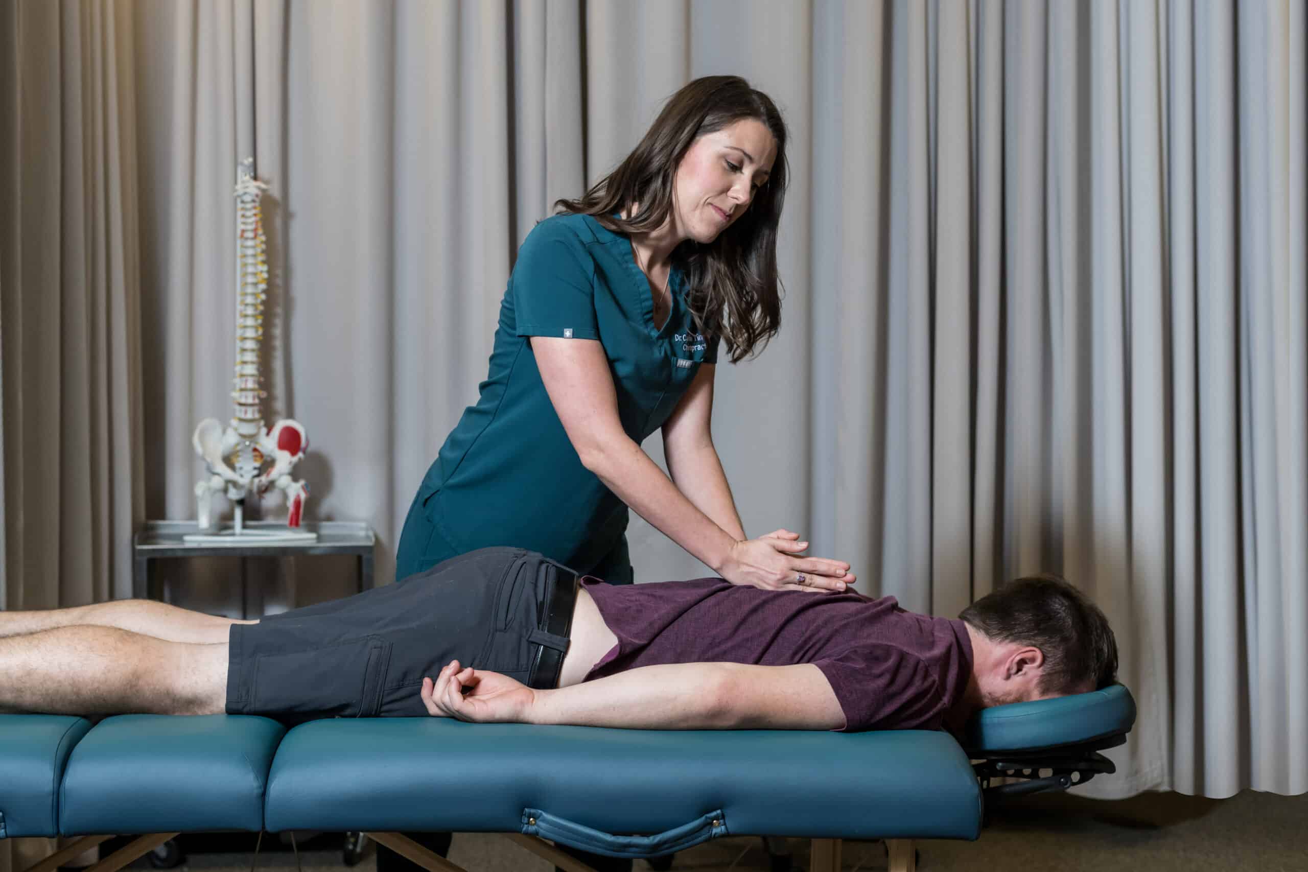 A chiropractor examining a male patient's spine on a treatment table.