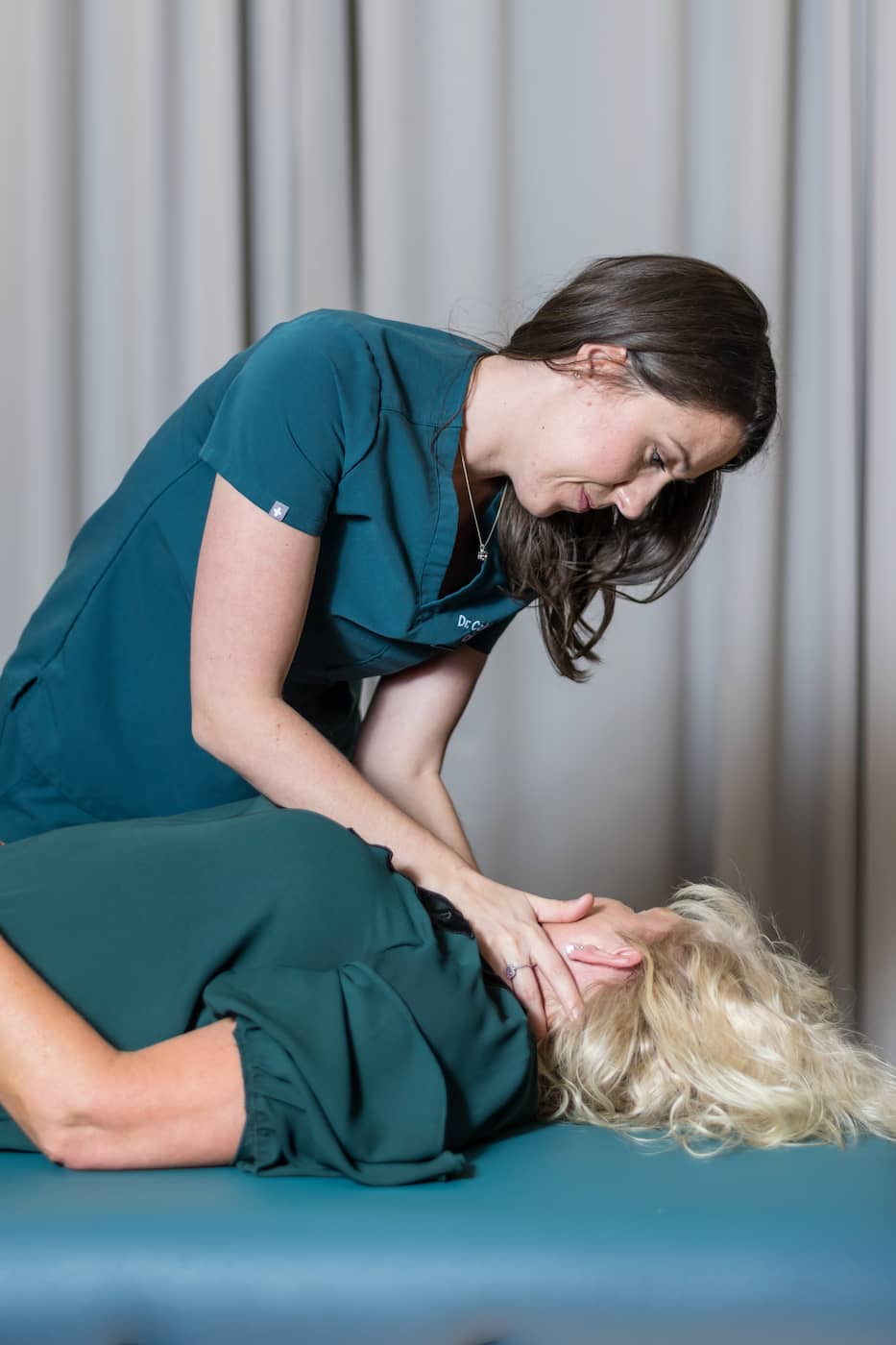 Chiropractor performing a neck adjustment on a patient lying face up.